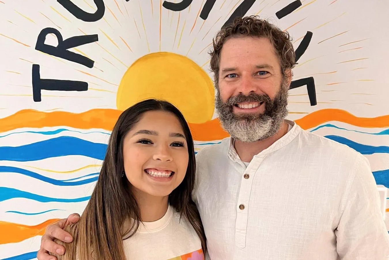 Smiling young woman and man posing together in front of a colorful mural featuring the sun and waves, representing True Smile Orthodontics' commitment to personalized orthodontic care.